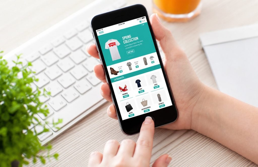 Person using a smartphone to browse an online shopping app with products, categories, and a spring sale collection.